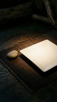 Blank white notebook with smooth stone on dark wooden surface with rustic logs overhead, suitable for journaling, writing, and creative projects.