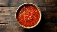 Fresh homemade salsa with diced tomatoes, onions, cilantro and chili peppers in rustic ceramic bowl on dark wooden background, top view, copy space.