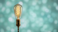 Vintage Edison bulb with warm glowing filament on soft turquoise bokeh background for creative lighting design and retro decor concepts.