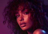 Young African American woman with curly natural hair in dramatic purple and blue lighting, glossy makeup and bare shoulders creating sensual beauty portrait.