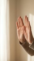 Two hands raised up in prayer or meditation gesture with warm natural lighting and soft beige background for wellness and spirituality concepts.