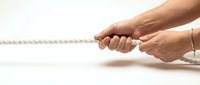 Two hands gripping thick rope in tug of war position showing teamwork, competition and strength concept for business motivation and challenge.