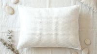Cream waffle weave pillow on white bedding with eucalyptus sprigs and decorative stones, ideal for bedroom, home decor, and lifestyle photography.