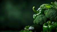 Fresh green vegetables including broccoli, cucumber, bell pepper and basil leaves arranged on dark background with copy space for healthy eating concept.