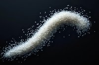 White sugar crystals scattered in curved motion against black background, creating dynamic powder trail effect. Macro food photography for culinary design.