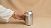 Woman hand with gold bracelet holding silver aluminum beverage can on beige background for product mockup and branding design.