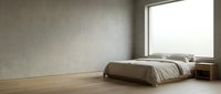 Minimalist bedroom interior with low platform bed, neutral bedding, wooden floor, concrete walls, and large window with natural light flooding empty space.