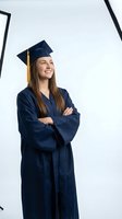 Confident young Caucasian woman graduate in navy blue cap and gown with crossed arms smiling proudly on white background for education designs.