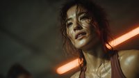 Young Asian woman with wet curly hair in tank top under warm neon lighting creating moody atmospheric portrait with orange glow and dramatic shadows.