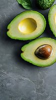 Fresh ripe avocado halves with pit and flesh on dark gray stone background, top view with copy space for healthy eating and food photography.
