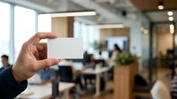 Businessman holding blank white business card in modern office environment with colleagues working in background.