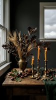 Autumn home decor with dried wheat, oak leaves in brass vase, lit candles on wooden table near window creating cozy seasonal atmosphere for fall decorating.