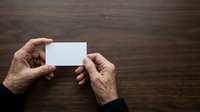 Senior adult hands holding blank white business card on wooden surface for mockup and branding purposes.