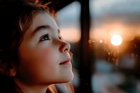 Young Caucasian boy with gentle smile gazing upward at sunset, warm golden light illuminating profile against blurred nature background, expressing wonder and hope.
