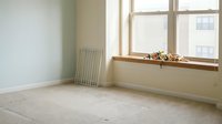 Empty room with beige walls, radiator, and large window with natural light, suitable for interior design, real estate, and renovation projects.
