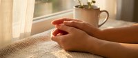 Woman hands holding red heart shape by sunny window with coffee mug and plant creating warm morning atmosphere for love and care concepts.
