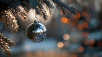 Shiny silver Christmas ornament hanging from pine branch with warm bokeh lights creating festive holiday atmosphere.