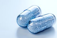 Transparent medical capsules filled with sparkling blue glitter particles on light background, pharmaceutical concept for healthcare and medicine innovation.