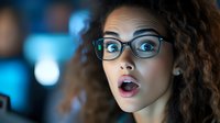 Young African American woman with curly hair and glasses expressing surprise with open mouth against blue bokeh background. Professional portrait capturing genuine emotion.