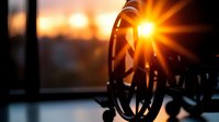 Silhouette of vintage wooden wagon wheel against dramatic sunset sky with sun rays bursting through spokes creating nostalgic rural atmosphere.