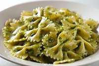 Delicious bow tie pasta with vibrant green pesto sauce and parmesan cheese served in white bowl, ready to eat Italian cuisine meal for food photography.
