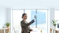 Businesswoman in brown blazer touching digital interface icons on glass window in modern office space with natural light and plants.