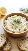 Creamy potato salad with fresh dill and black pepper in wooden bowl, served with lemon slices and toasted bread for appetizer or side dish.