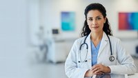 Confident female doctor in white coat with stethoscope standing in modern hospital setting, healthcare professional ready for patient care.