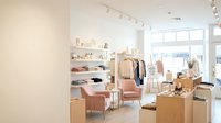 Modern minimalist retail clothing store interior with neutral tones, wooden fixtures, pink chairs and organized merchandise display for fashion boutique design.