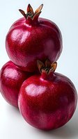 Fresh ripe pomegranates with deep red skin and crown-shaped tops on white background, macro shot showing detailed texture and natural shine. Suitable for food marketing.