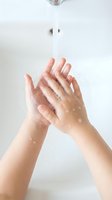 Woman washing hands with soap and water droplets under bathroom faucet for hygiene and cleanliness routine in modern white sink.