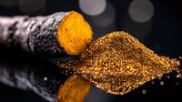 Fresh turmeric root cut to reveal vibrant orange interior next to golden powder on black reflective surface with bokeh lights in dark background.