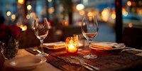 Elegant table setting with wine glasses and candlelight creating romantic ambiance in restaurant with blurred city lights background.