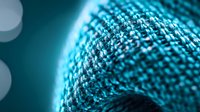 Macro shot of knitted winter hat texture in turquoise blue color with soft bokeh lights background showing detailed wool or yarn pattern structure.
