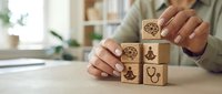 Healthcare professional arranging wooden blocks with medical symbols including stethoscope and wellness icons on desk for patient education and treatment planning.