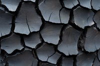 Dramatic close-up of dark cracked earth texture showing deep fissures and geometric patterns. Natural abstract background with rough dried mud surface in grayscale tones.