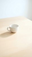 Empty white ceramic mug on wooden table with natural light and shadow, isolated on neutral background for product mockup and design use.