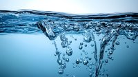 Dynamic underwater scene with air bubbles rising through clear blue water, split-level view showing surface ripples and submerged turbulent flow patterns.