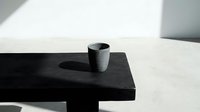 Minimalist ceramic cup on black wooden table with soft natural light casting shadows, suitable for interior design, lifestyle, and product photography projects.