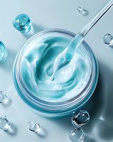 Luxurious turquoise cosmetic cream in glass jar with metallic spatula and water drops on light background, top view macro photography for skincare products.