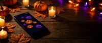 Halloween tarot card reading setup with smartphone displaying mystical symbols, candles, pumpkins and autumn leaves on rustic wooden table for seasonal divination.