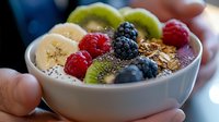Fresh acai smoothie bowl topped with sliced banana, kiwi, berries, chia seeds and granola in white ceramic bowl. Healthy breakfast concept.