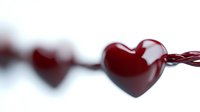 Red glossy heart shapes connected by thin string against white background, shallow depth of field creates romantic blur effect. For Valentine's Day designs and love concepts.