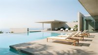 Modern luxury villa with infinity pool and wooden deck chairs overlooking serene landscape at sunset for vacation rental and real estate marketing.