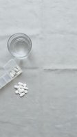 White pills spilled from bottle with glass of water on marble surface for medication and healthcare concepts.