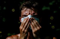 Sick man sneezing into tissue with virus particles floating around, showing cold flu symptoms and seasonal illness concept for health awareness campaigns.