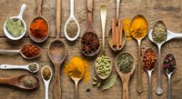 Colorful spices and herbs arranged in wooden spoons on rustic table. Cooking ingredients including turmeric, paprika, cinnamon, cardamom for culinary recipes.