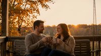 Young couple enjoying wine on porch swing during golden hour autumn evening, romantic date night atmosphere with warm sunset lighting and fall foliage.