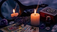 Mystical fortune telling setup with tarot cards, burning candle, crystal ball mirror, gemstones and ornate wooden box for spiritual divination practices.