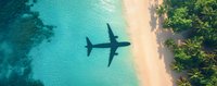 Airplane shadow over turquoise ocean water and sandy tropical beach with palm trees, aerial view capturing tranquil paradise destination and travel concept.
